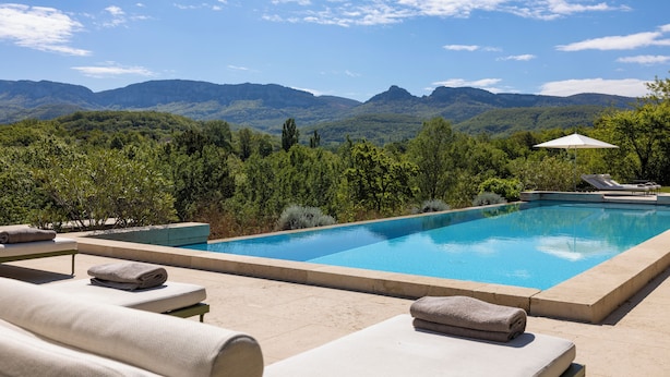 A rectangular swimming pool with a clear blue water surface, surrounded by lounge chairs and a white umbrella.