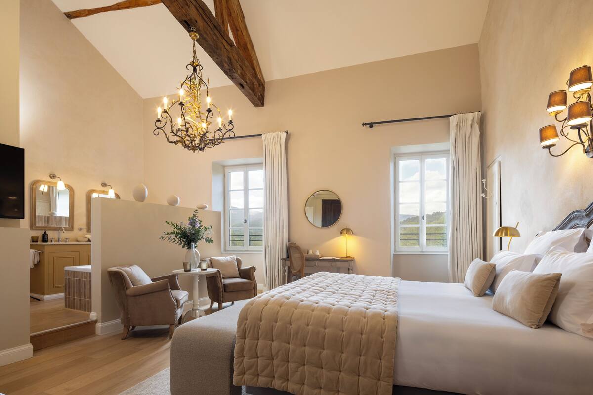 A spacious bedroom with a large bed, a chandelier, and a view of the outdoors through the window.