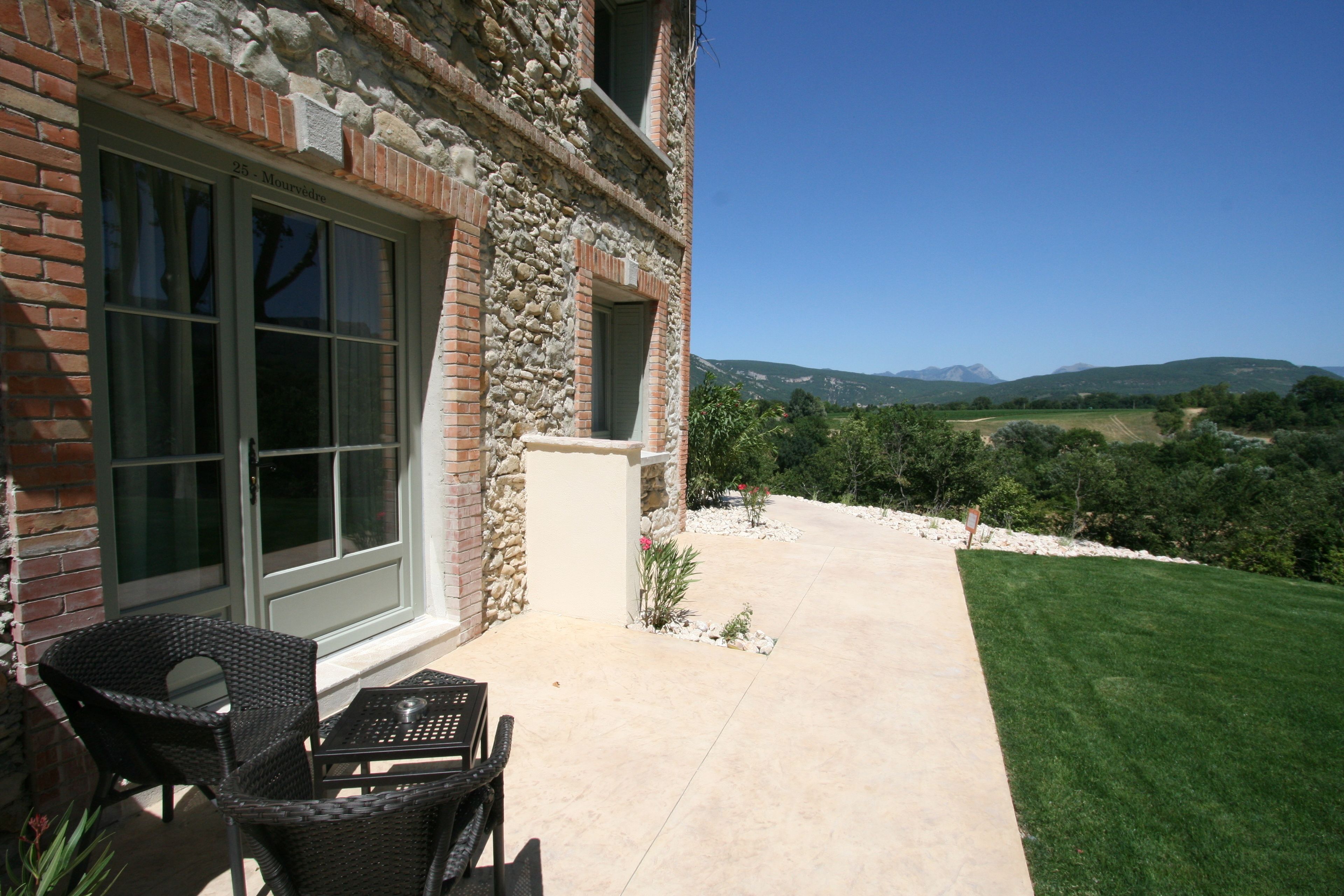 Une terrasse dotée de meubles en osier, d’un mur en pierre et offrant une vue sur un paysage verdoyant avec des collines.