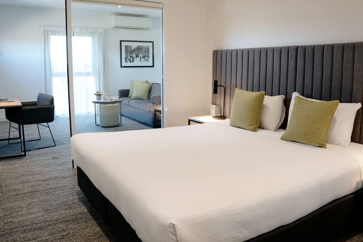 A hotel room with a large bed, a desk, a chair, and a sofa.