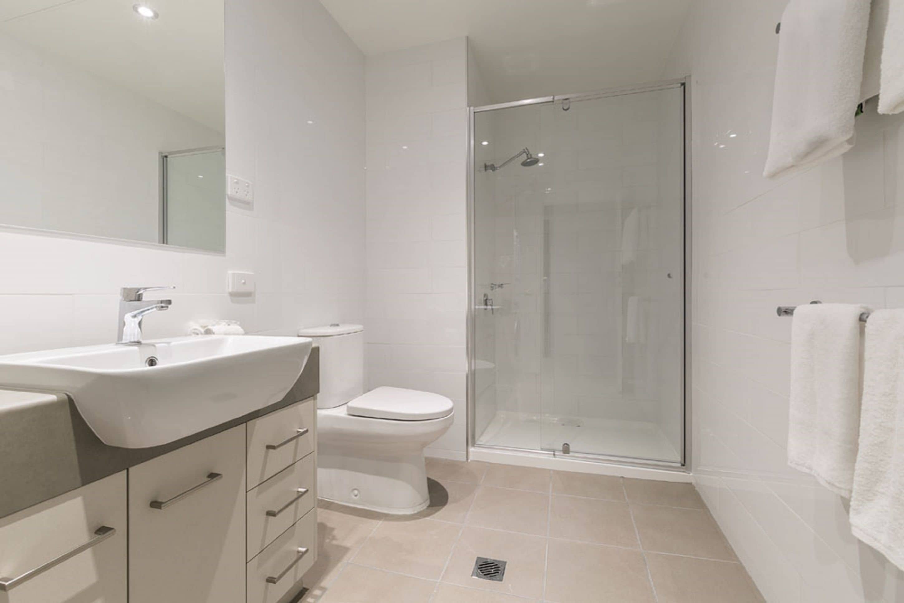 Un baño moderno con ducha de vidrio, lavamanos blanco y retrete.