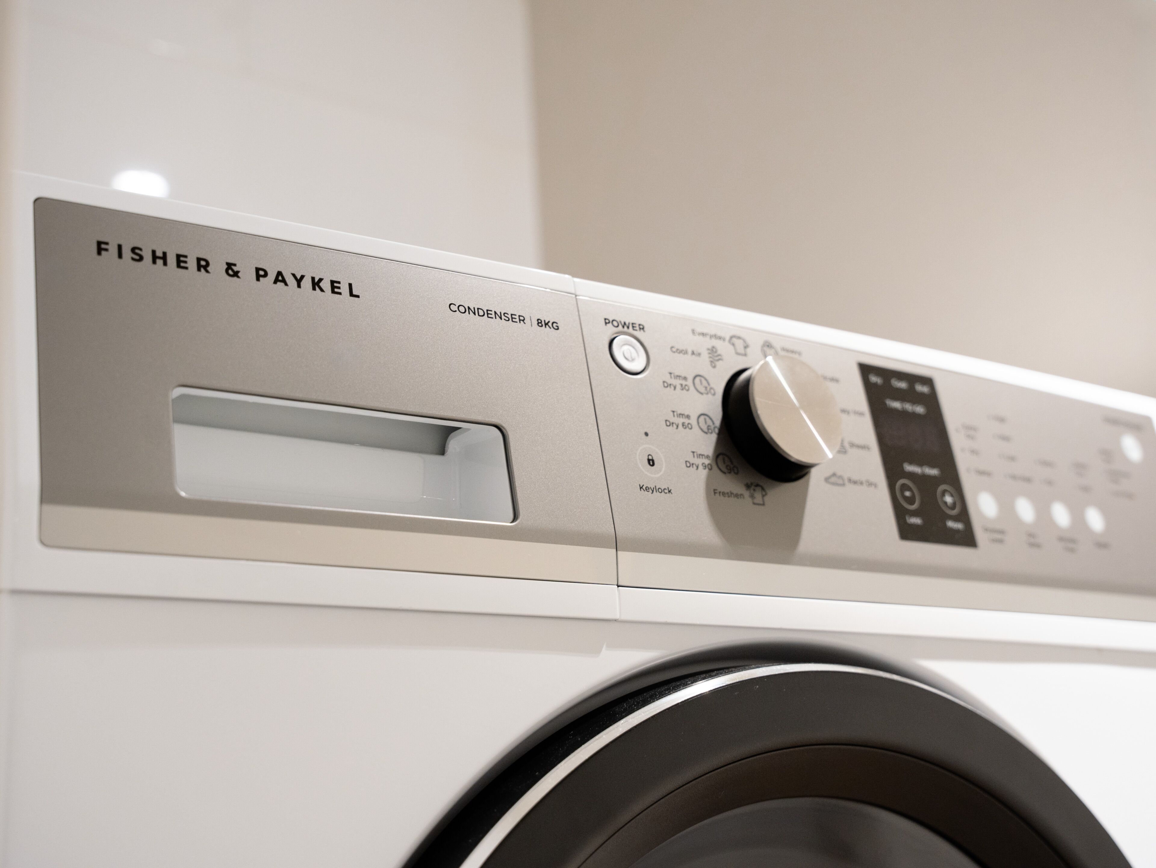 En Fisher & Paykel vaskemaskine med kontrolpanel, der viser en tænd/sluk-knap, tidsindstillinger og en låsefunktion.