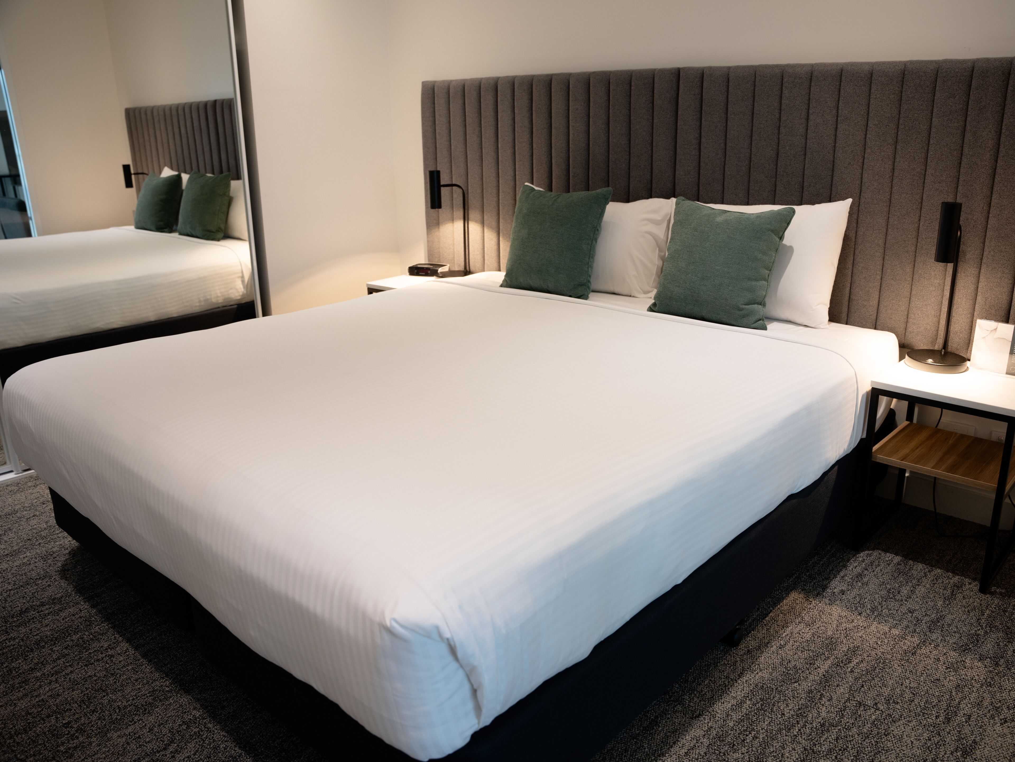 A hotel room with a large bed, a bedside table with a lamp, and a mirror on the wall.