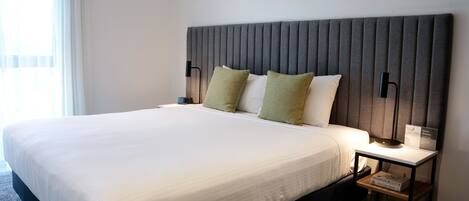A neatly made bed with white linens, a grey headboard, and two bedside lamps.