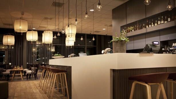 Eine moderne Bar mit einer zentralen Barinsel, Barhocker, hängenden Pendelleuchten und einer Weinauslage.