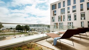 Ein modernes Gebäude mit einem Glasbalkon mit Blick auf eine Marina und einem klaren Himmel.