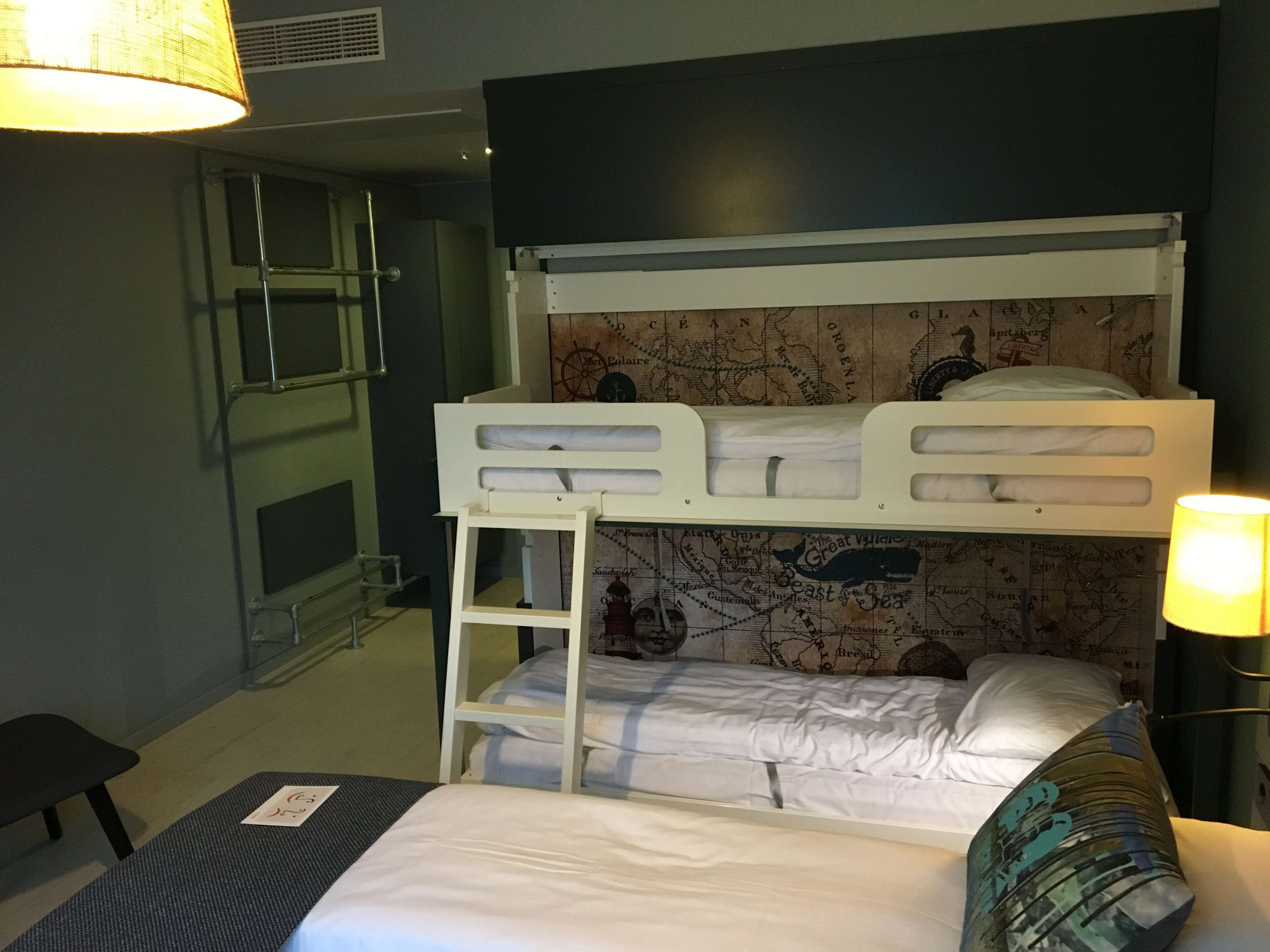 Ein Schlafzimmer mit Etagenbetten, einem Kopfstück mit Weltkarten-Motiv, einer Himmellaune, einem Schreibtisch und einer Lampe.