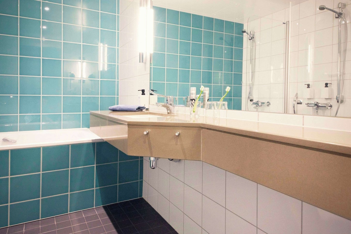 Une salle de bain avec des carreaux de couleur turquoise, un lavabo blanc et un miroir au-dessus du lavabo.
