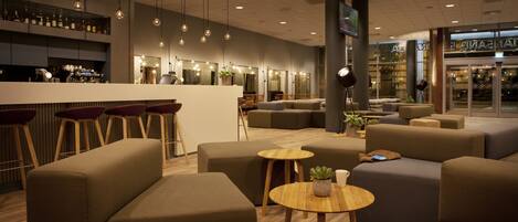 Un área de lounge moderna con sofás, una barra y un espacio de estar con mesas redondas.