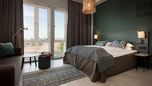 Ein Schlafzimmer mit einem großen Bett, einem Schlafsofa, einem kleinen Tisch, einer Lampe und Blick auf die Stadt durch das Fenster.