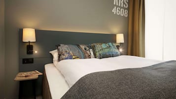 A hotel room with a large bed, two bedside lamps, a nightstand with a newspaper, and a wall with the number "4608".