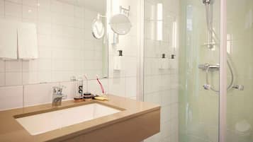 A bathroom with a beige sink, two mirrors, a glass shower enclosure, and a white towel hanging on the wall.