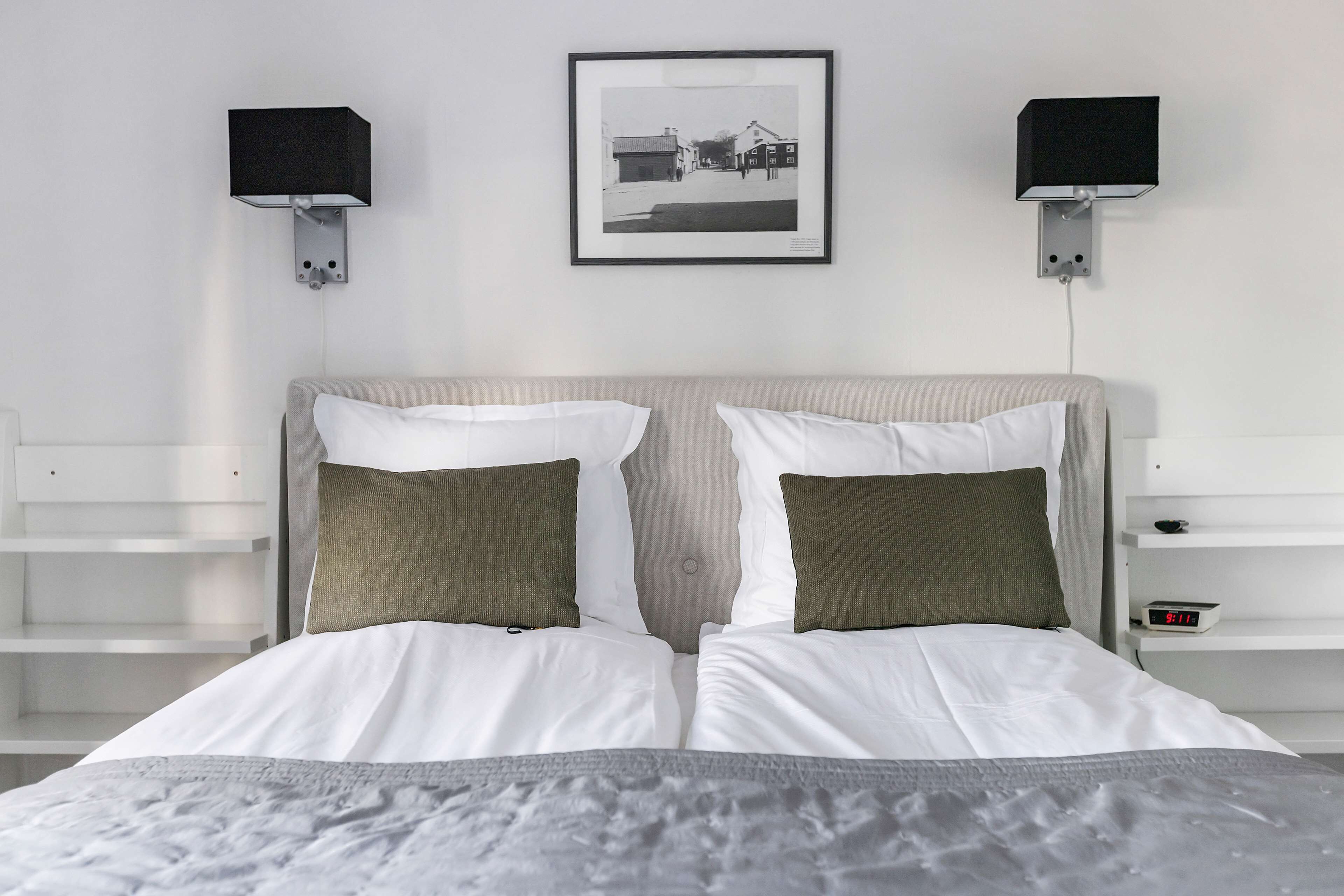 A neatly made double bed with white and green pillows, a grey blanket, and a framed picture above.