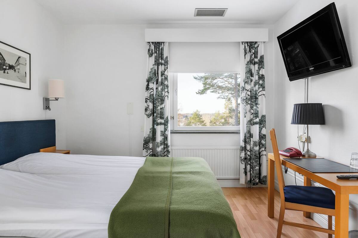 A hotel room with a bed, a desk, a chair, a television, and a window with curtains.