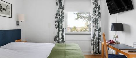 A hotel room with a bed, a desk, a chair, a television, and a window with curtains.