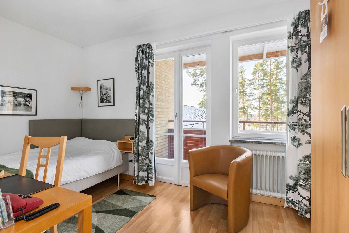 A bedroom with a bed, a chair, a table, and a window with curtains.