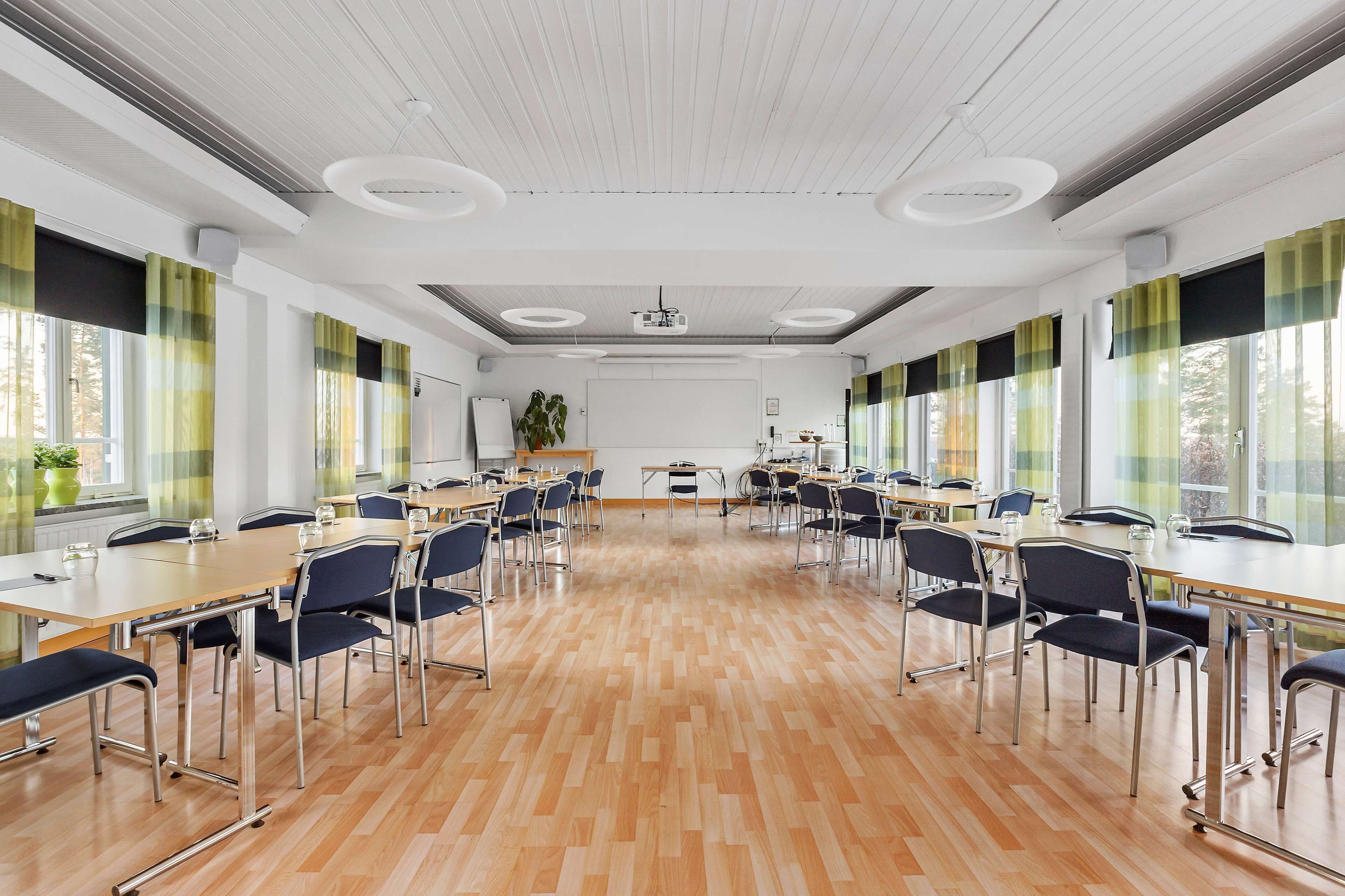 Une salle de conférence avec une longue table, des chaises, un projecteur et de grandes fenêtres équipées de rideaux.