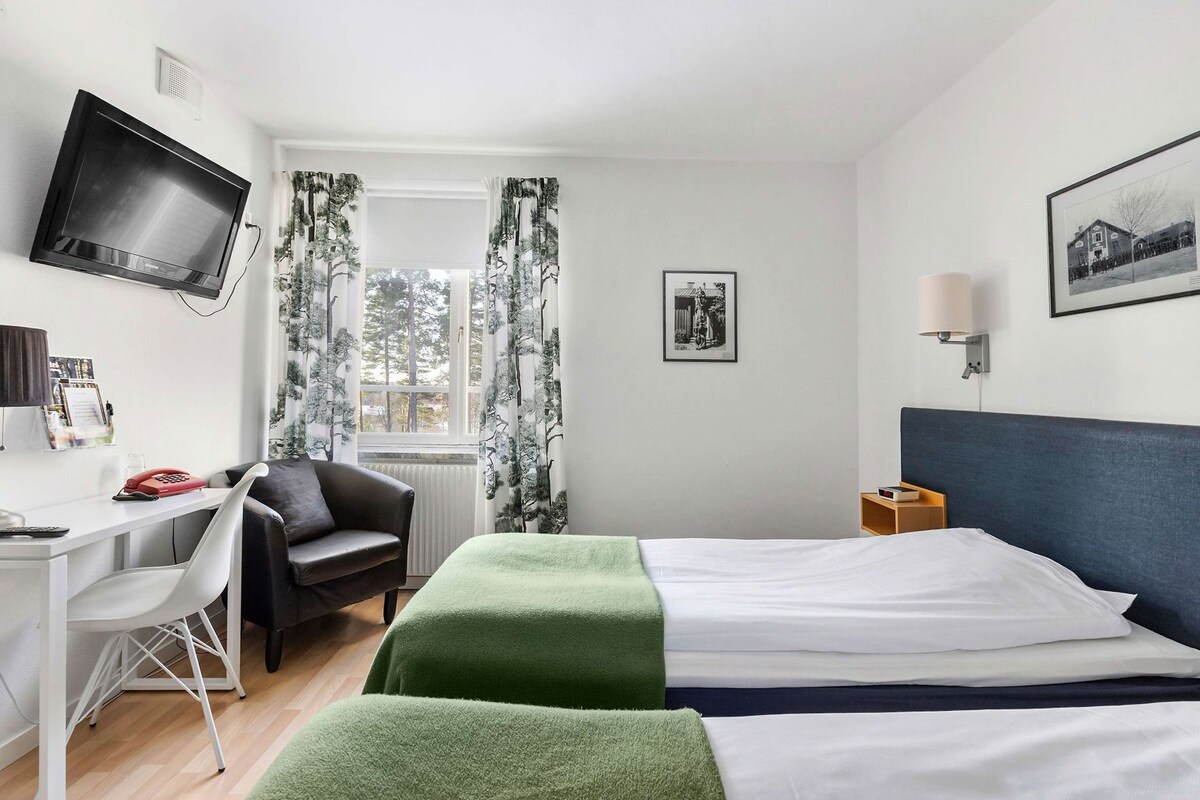 A hotel room with a bed, a desk with a chair, a television, and a window with curtains.