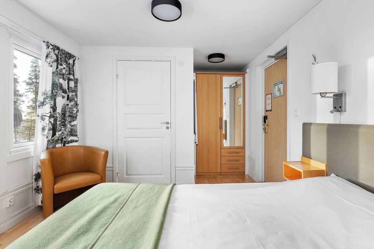 A bedroom with a bed, a chair, a wardrobe, and a mirror.