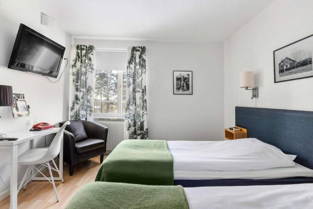 A hotel room with a bed, a desk, a chair, a TV, and a window with curtains.