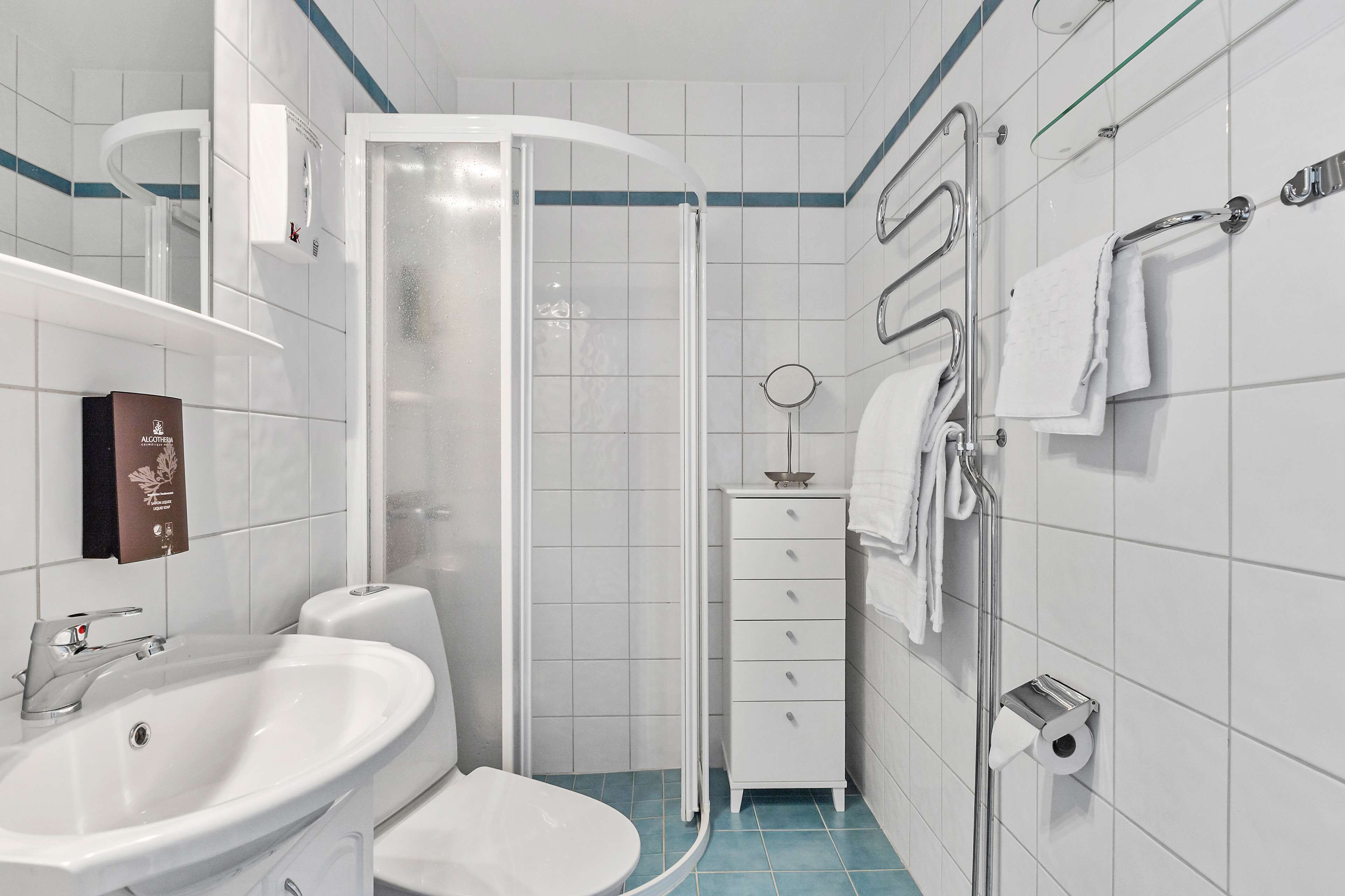 Un baño moderno con un lavamanos, inodoro y ducha blancos. Hay un perchero y un dispensador de jabón en la pared.