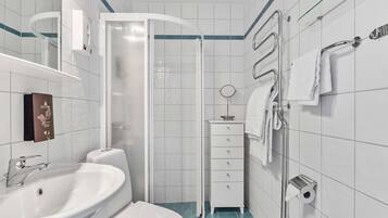 Un baño moderno con un lavamanos, inodoro y ducha blancos. Hay un perchero y un dispensador de jabón en la pared.