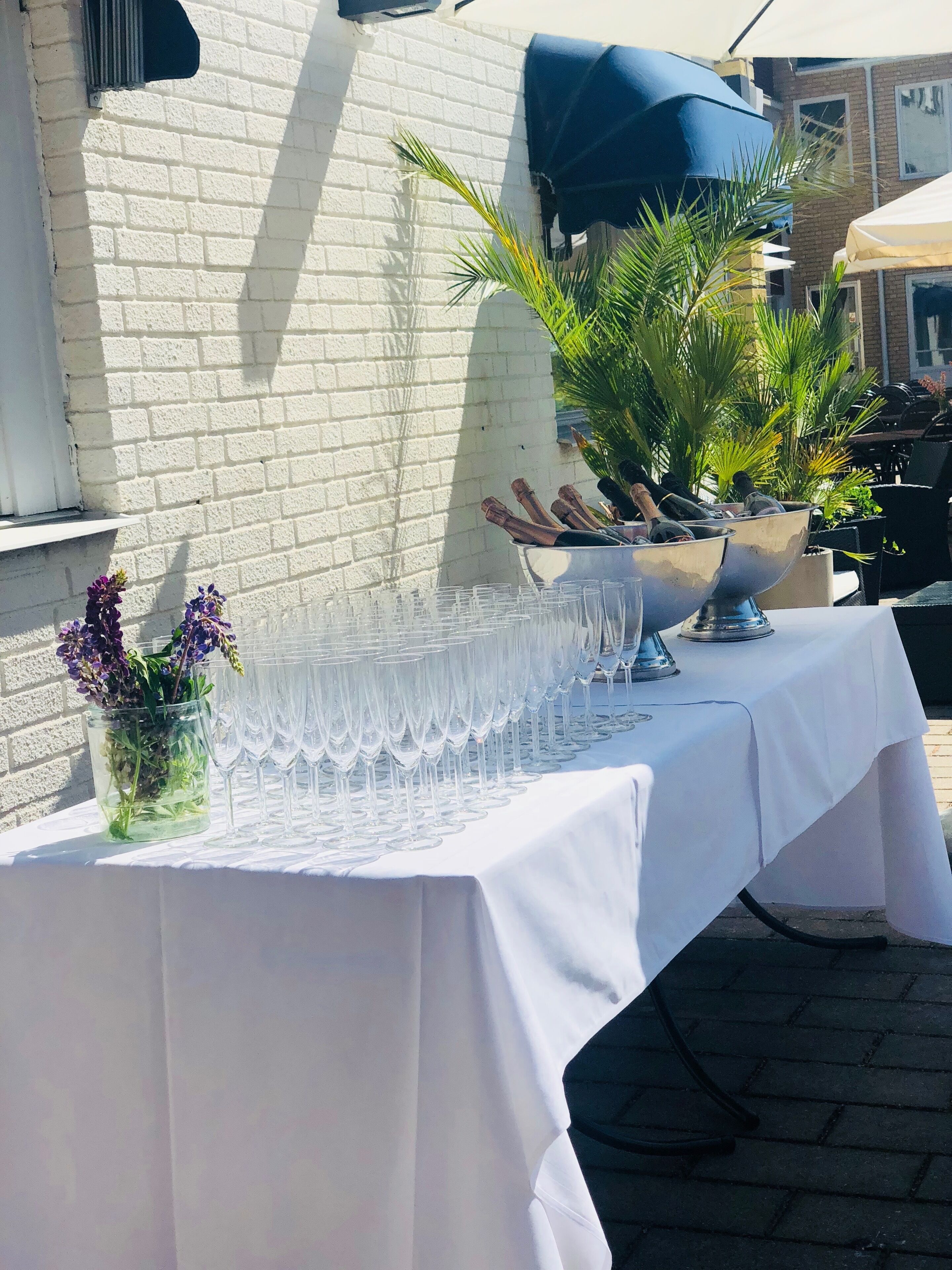 A table set outdoors with a white tablecloth, a bowl of champagne, and a vase of flowers.