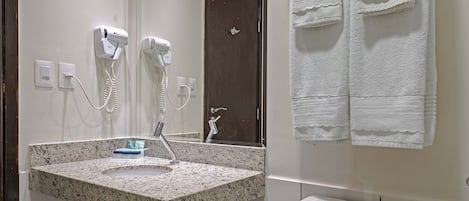 A bathroom with a sink, mirror, towel rack, toilet, and a trash bin.