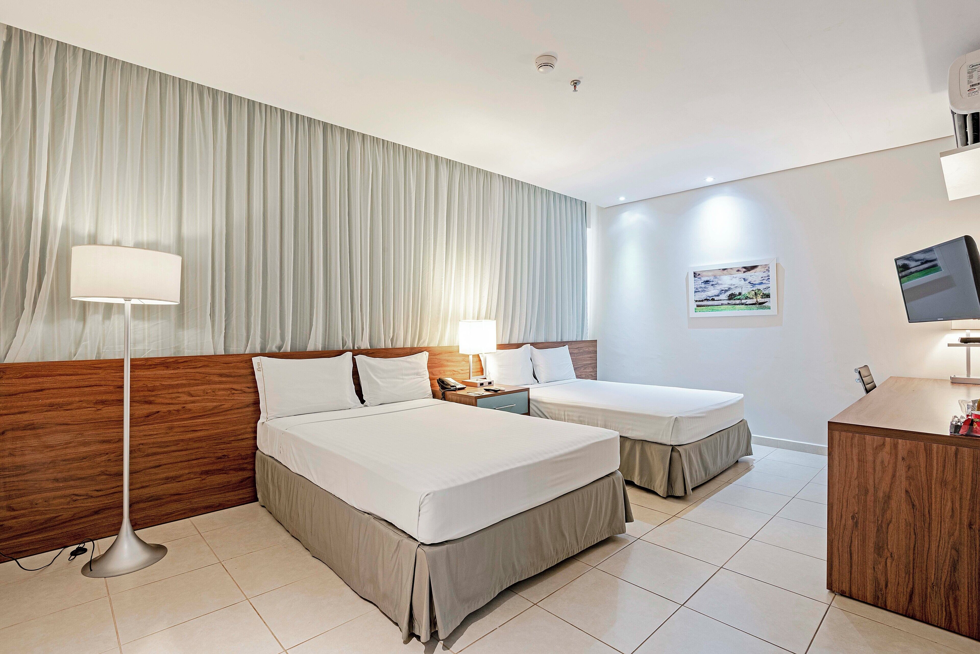 A hotel room with a large bed, a smaller bed, a desk, a lamp, a phone, and a picture on the wall.