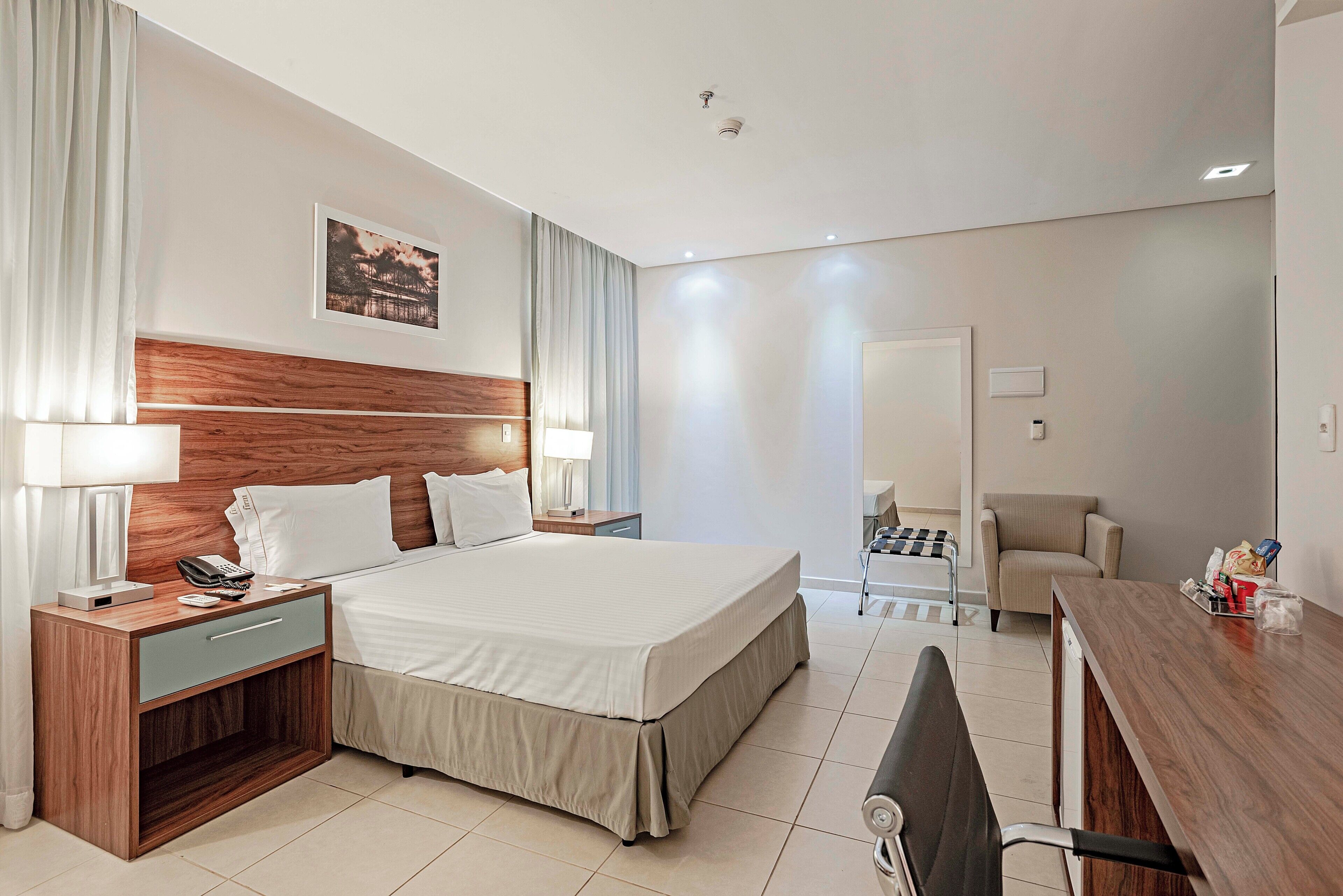 A modern hotel room with a large bed, bedside tables, a desk, and a chair.