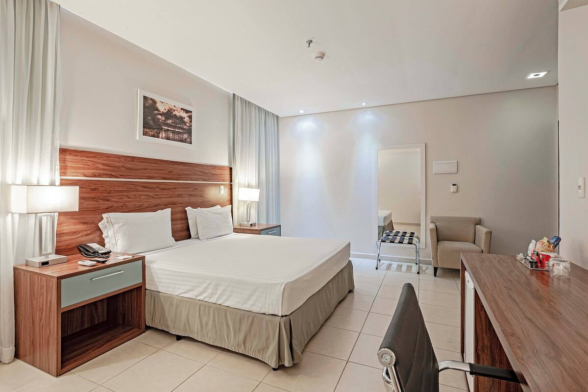 A modern hotel room with a large bed, bedside tables, a desk, and a chair.