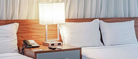 A hotel room with two beds, a nightstand with a lamp, a phone, and a small drawer.