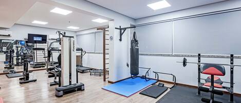 Un gimnasio con equipos de ejercicio variados, un saco de boxeo y una banca para pesas.