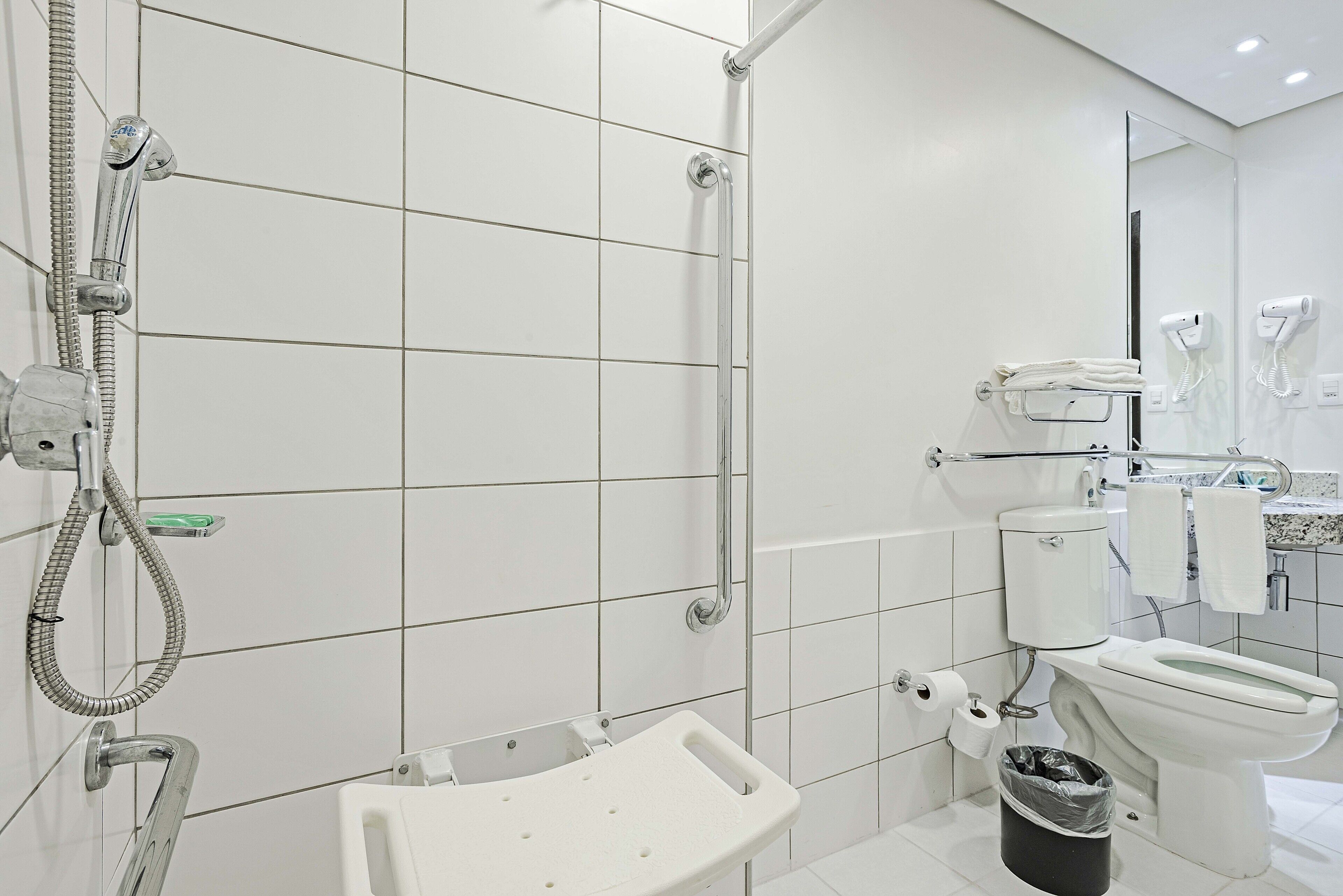 A modern bathroom with white tiles, a shower with a handheld showerhead, a toilet, and a bidet.