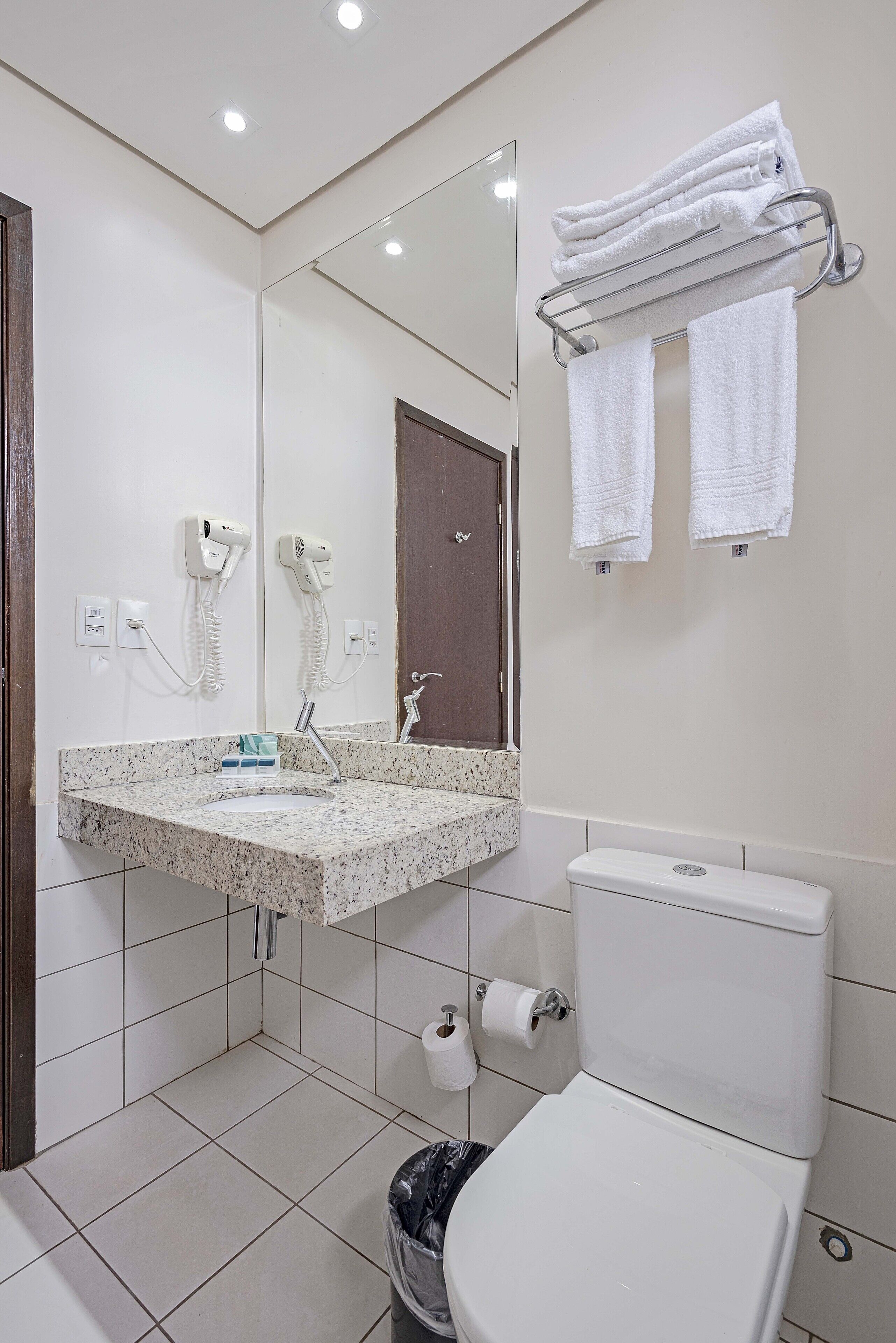 Une salle de bain équipée d’un lavabo, d’un miroir, d’un porte-serviettes, de toilettes et d’une poubelle.