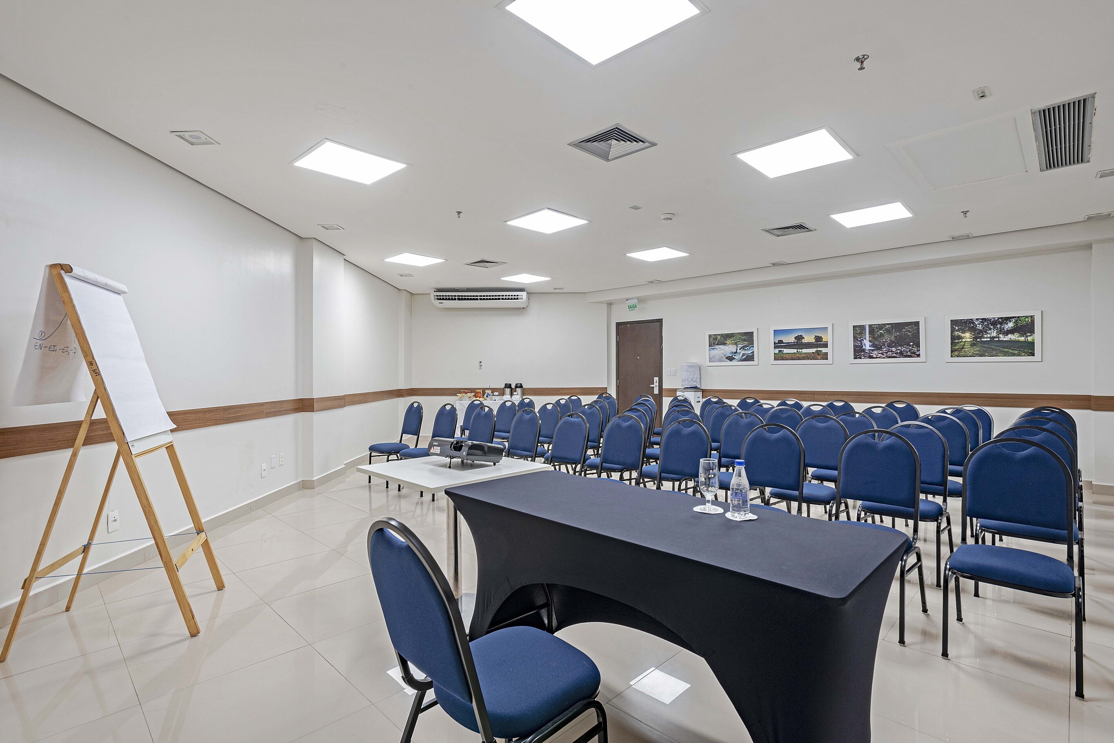Ein Konferenzraum mit einem langen Tisch, blauen Stühlen, einer Whiteboard und gerahmten Bildern an der Wand.