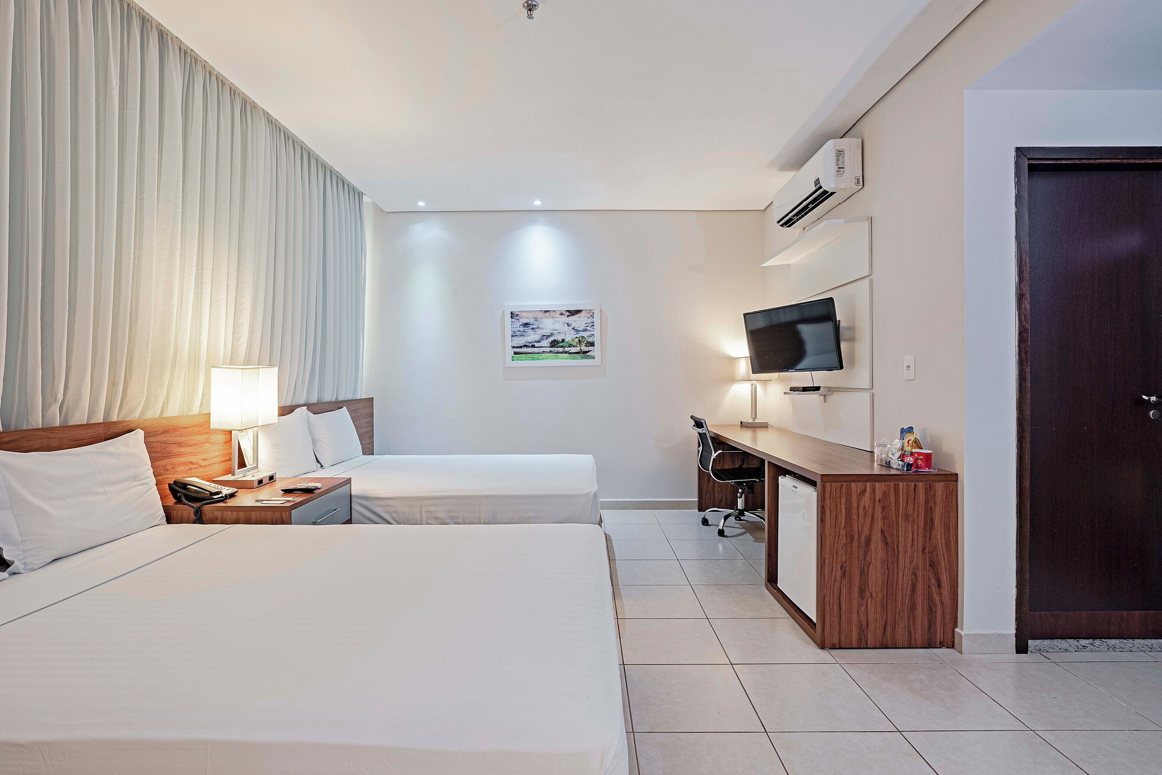 A hotel room with two beds, a desk, a television, and a door.