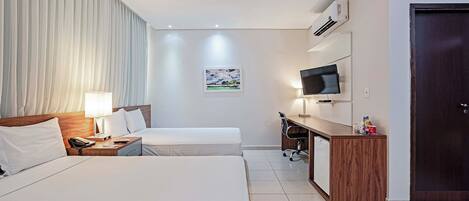 A hotel room with two beds, a desk, a television, and a door.