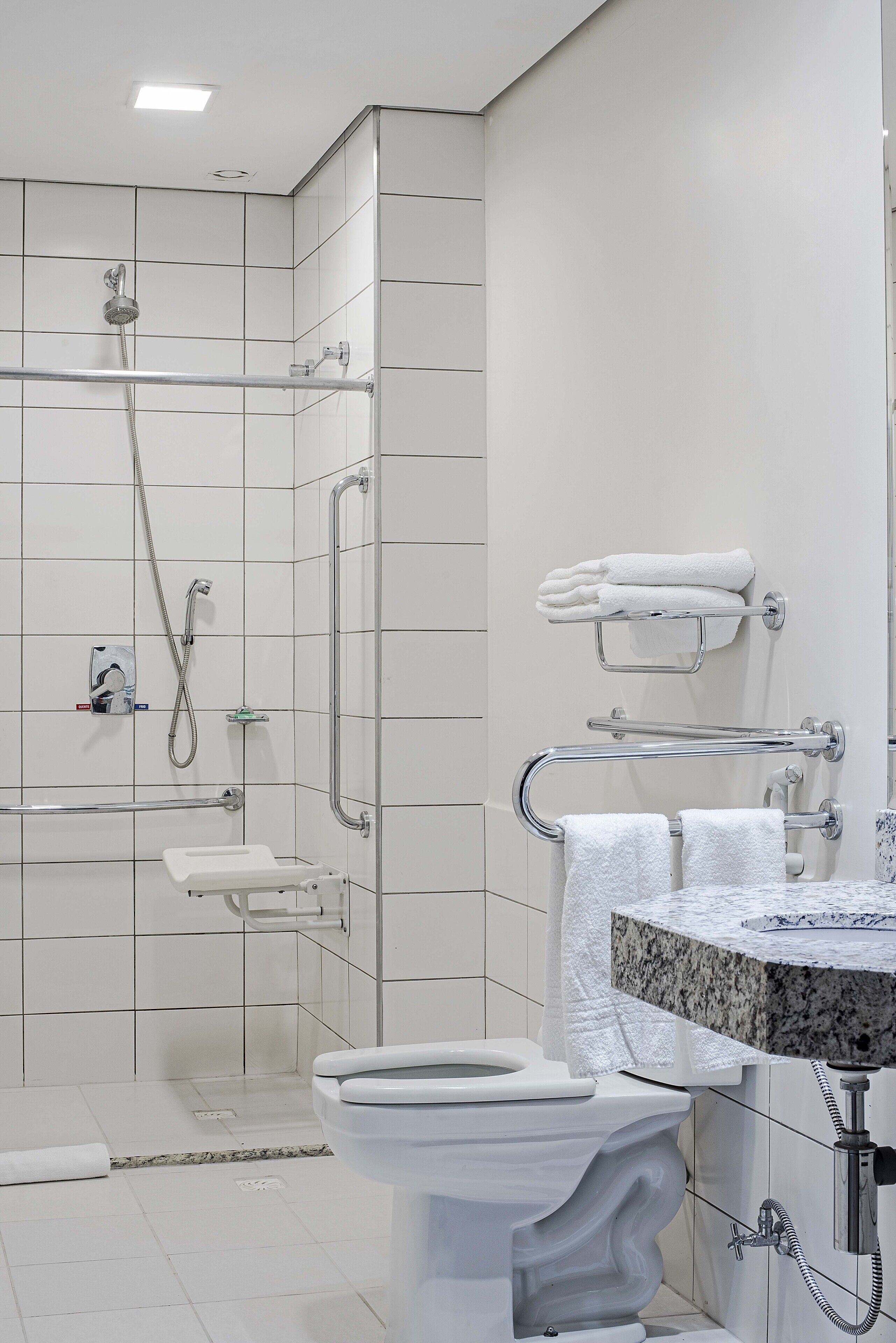 Un baño moderno con ducha a nivel, barras de apoyo, inodoro y lavabo con encimera de mármol.