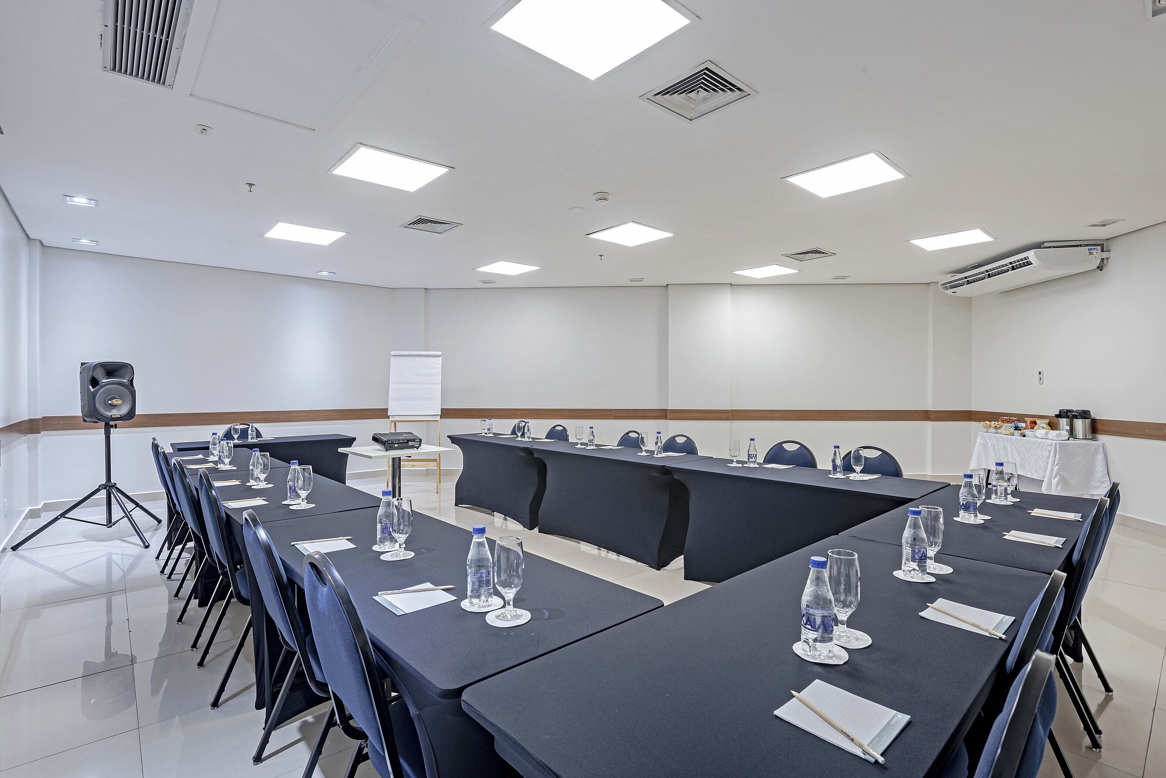 Un salón de conferencias con una larga mesa, sillas, botellas de agua y una pizarra.