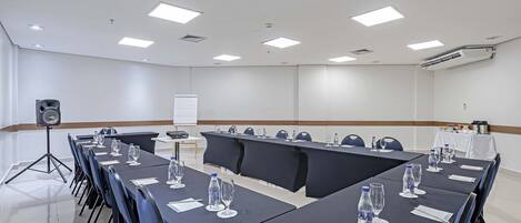 Un salón de conferencias con una larga mesa, sillas, botellas de agua y una pizarra.