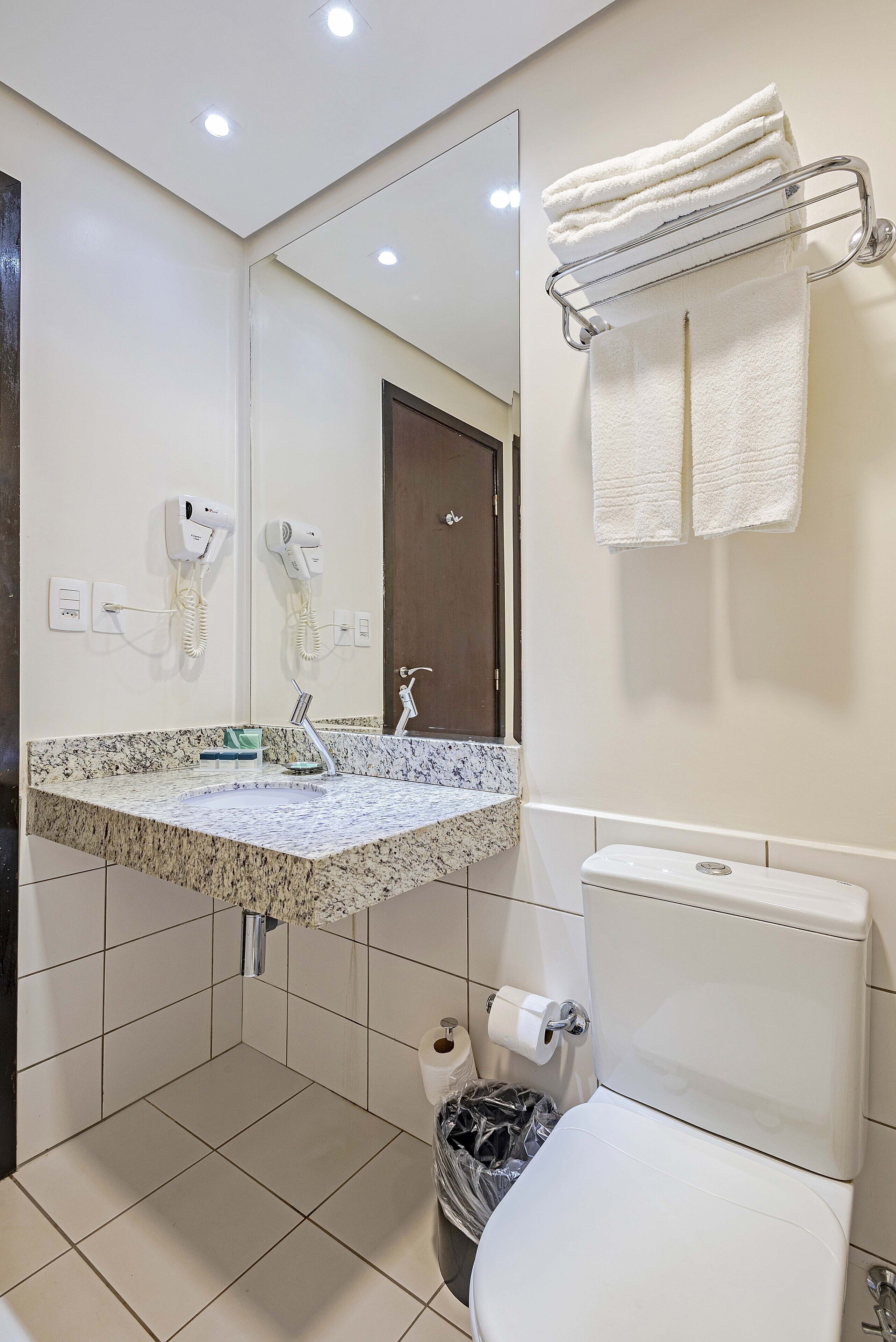 A bathroom with a marble sink, a toilet, a trash bin, and a towel rack with towels.