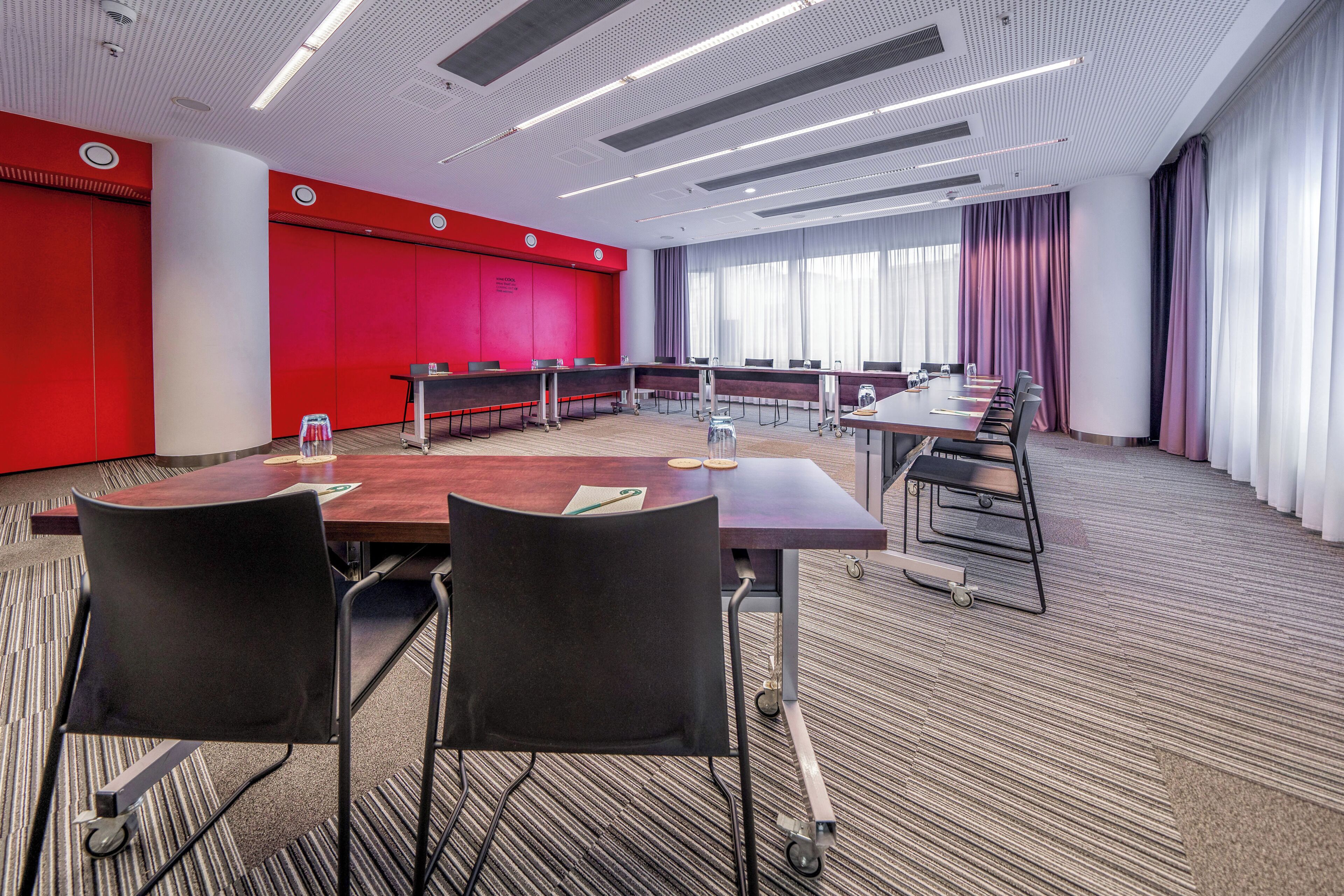 A conference room with a long table, multiple chairs, and a red accent wall.