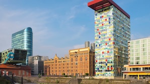 Un paisaje urbano con una variedad de estilos arquitectónicos, incluyendo un edificio moderno de vidrio, un edificio colorido con una fachada peculiar y un edificio tradicional de ladrillo.