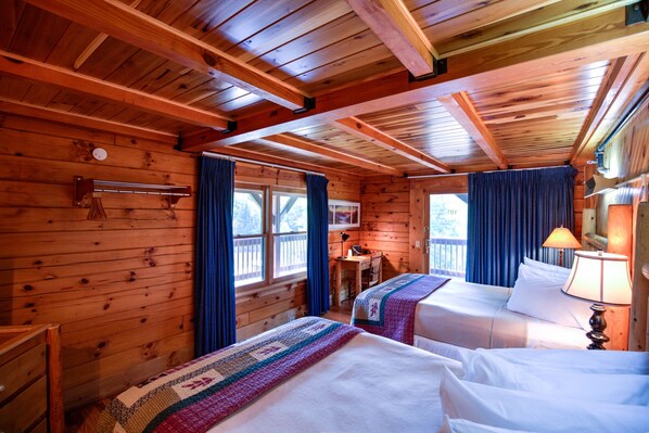 A cabin with two beds, wooden walls, a desk, and a window with curtains.