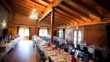 A large, rustic dining hall with wooden beams and a chandelier, tables set for a formal meal.
