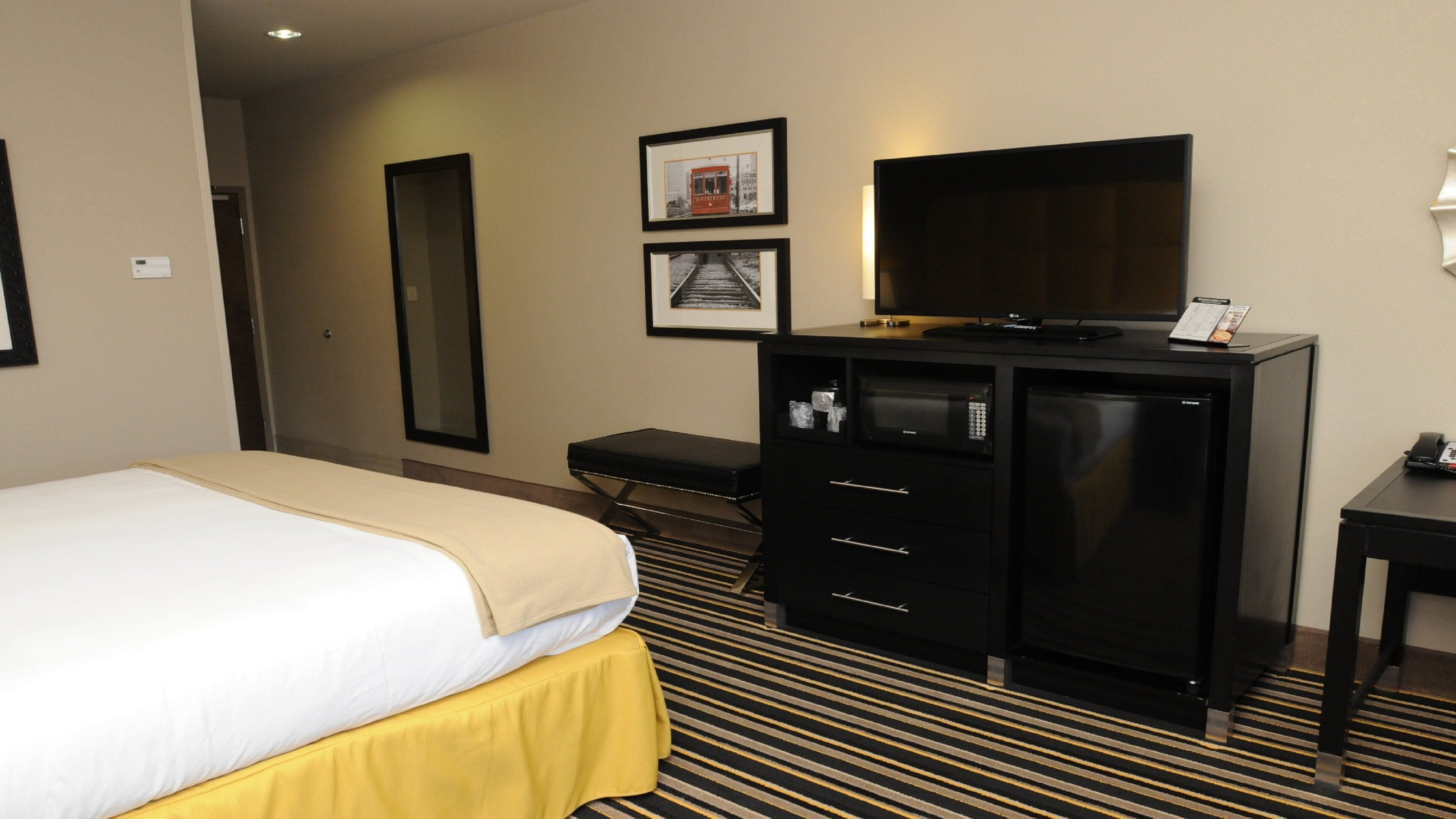 A hotel room with a bed, a desk, a television, and a minibar.