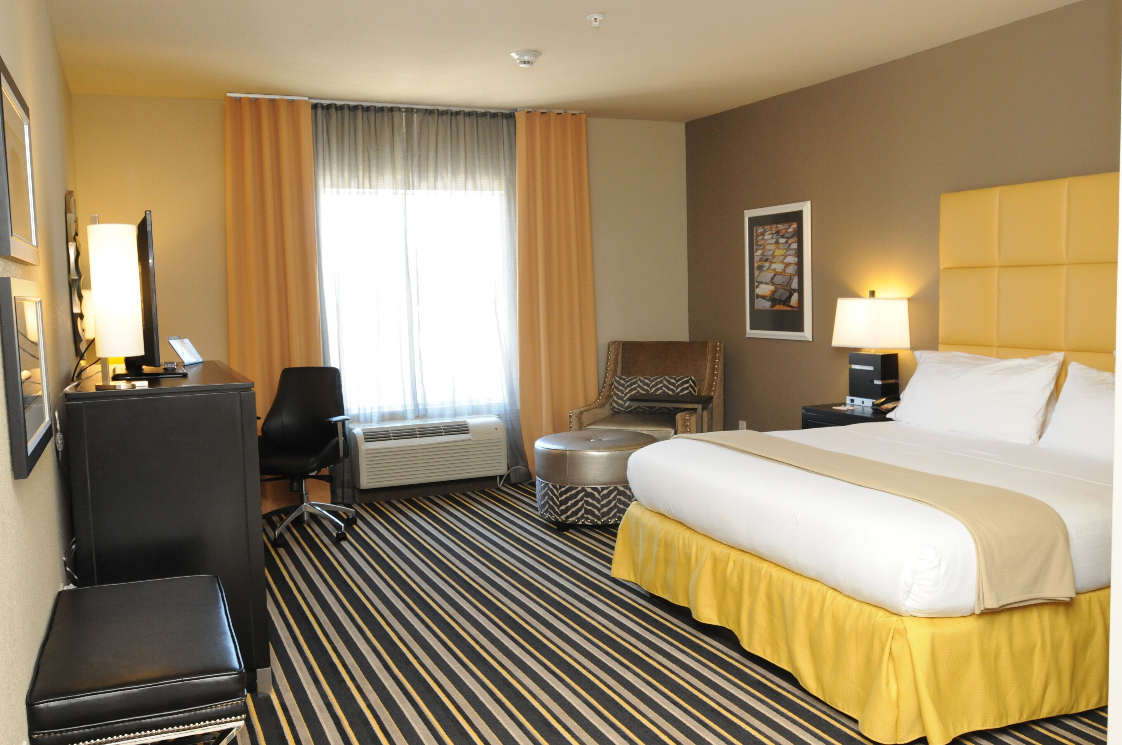 Ein Hotelzimmer mit einem Bett, einem Schreibtisch, einem Stuhl, einer Klimaanlage und einem Vorhangfenster.