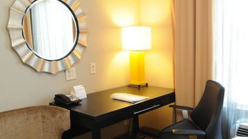 A hotel room with a desk, a chair, a lamp, a telephone, and a mirror.