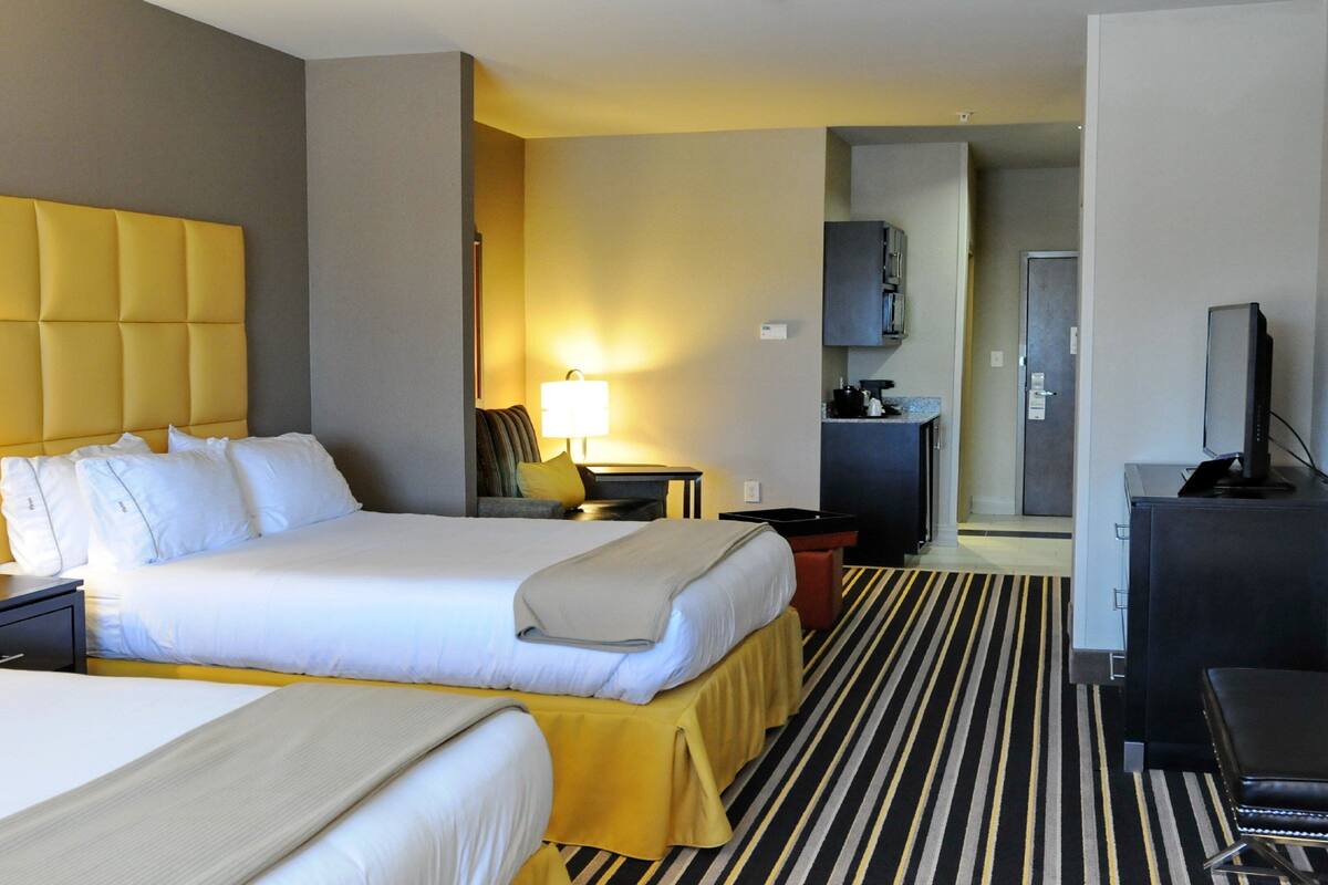 A hotel room with two beds, a desk, a chair, a television, and a kitchenette.